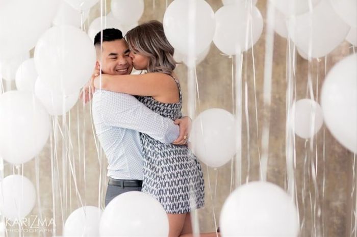 couple announcing engagement hugging balloons