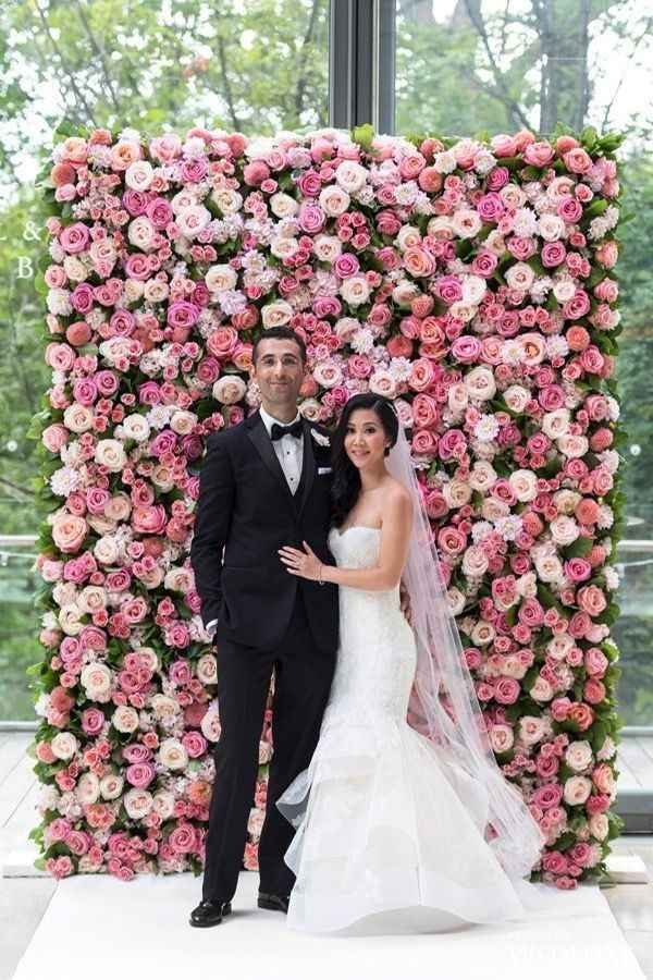 couple standing in front of flower wall, pink flower wall 