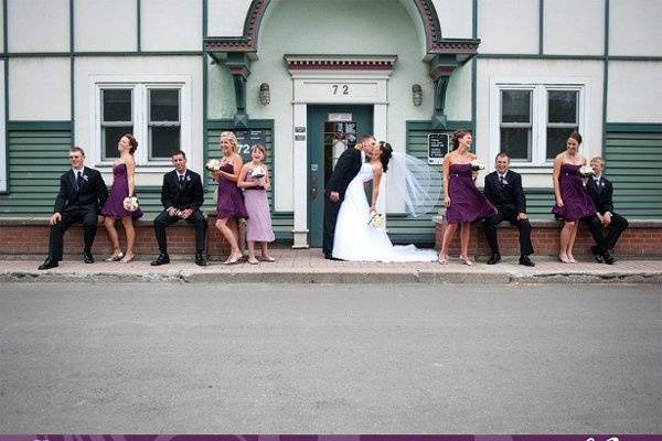 Bridal party standing in a line outside of a building, bride and groom kissing.jpeg