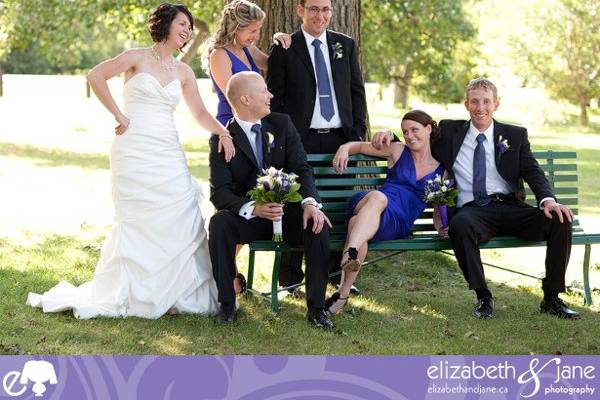 The wedding party sitting on a bench laughing.jpeg